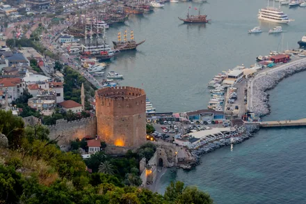 Det røde tårnet og havna i Alanya i skumringen, med utfluktsbåter ved kaia